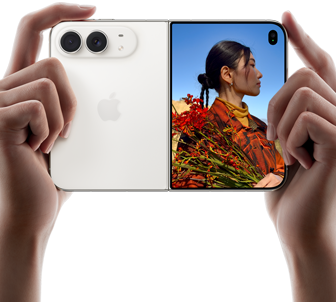 iPhone Duo, kleur Sterrenwit, met twee handen vastgehouden in liggende stand, opengevouwen, linkerkant met 48-MP Dual Fusion-camera’s aan de achterkant, op het buitendisplay rechts staat iemand die wordt gefotografeerd en dankzij Duo Preview tegelijkertijd zichzelf kan zien
