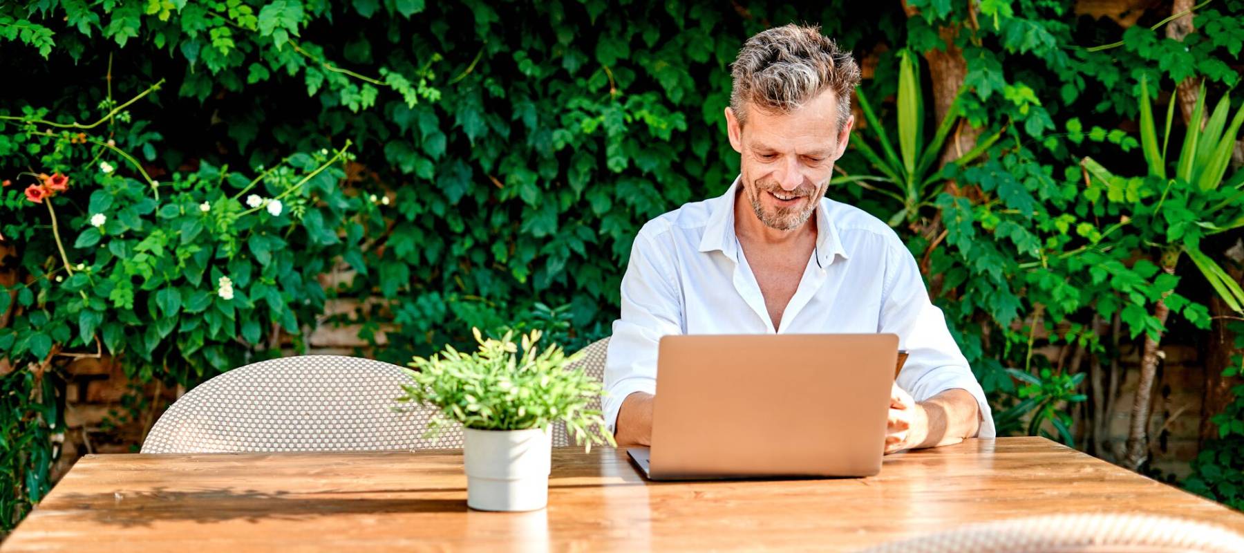 Man zit aan tafel met laptop en planten op de achtergrond